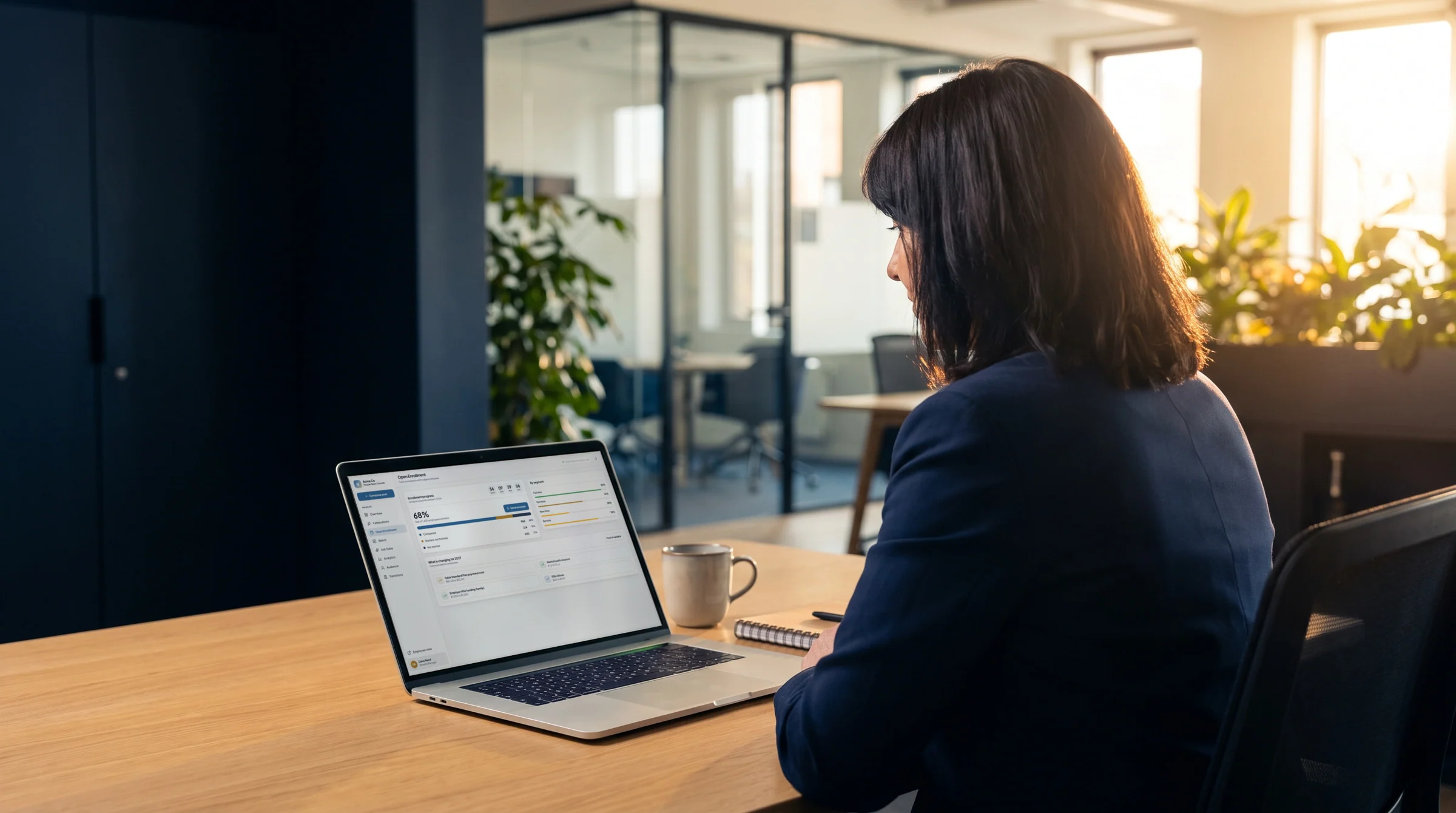 An HR manager at her desk in an open-plan office, the HR console open on her laptop