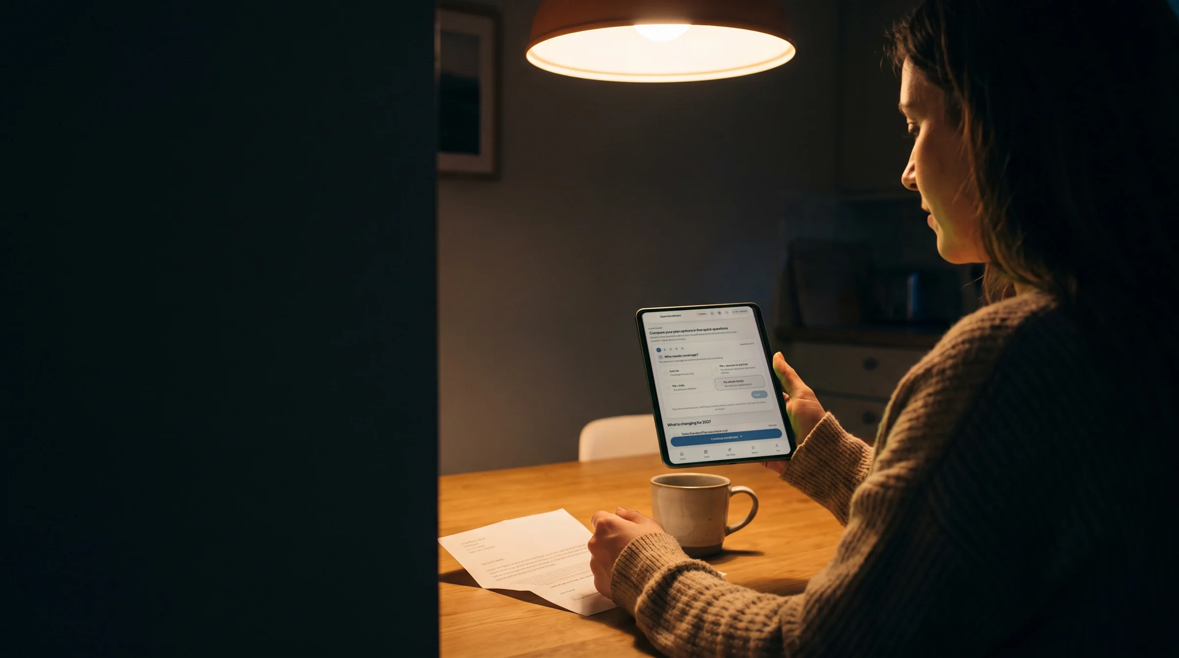 A woman at her kitchen table in the evening, comparing plan options in Plan Finder on her tablet