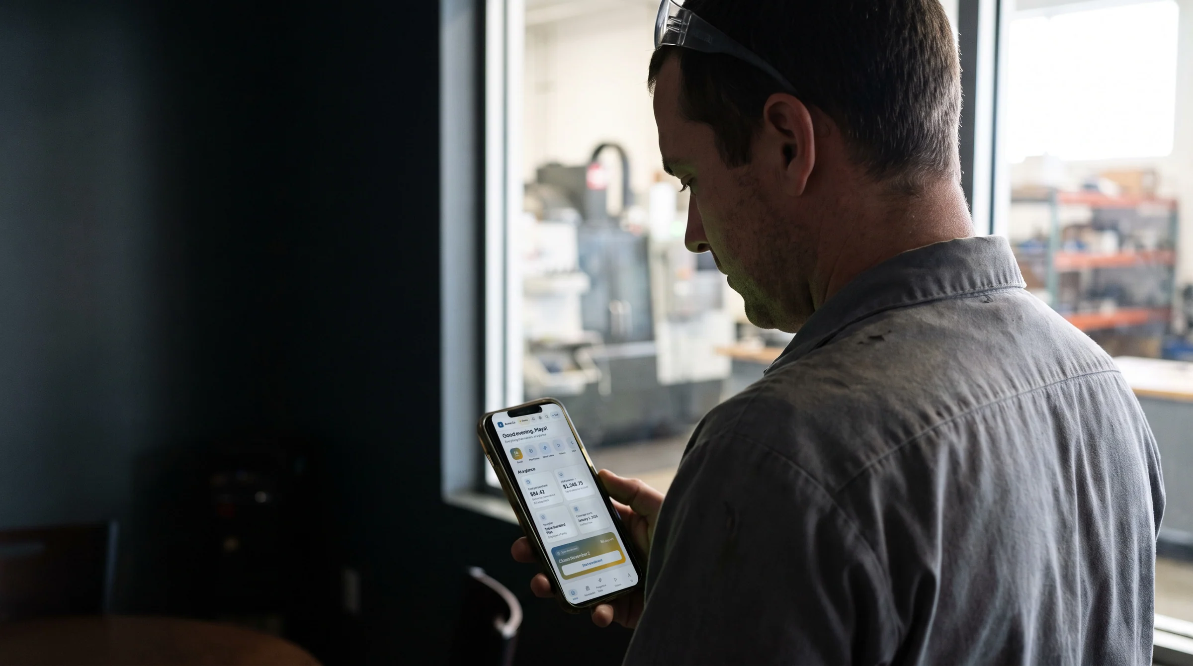 A technician in a plant break area, reading the benefits hub on his phone, its navigation in Spanish